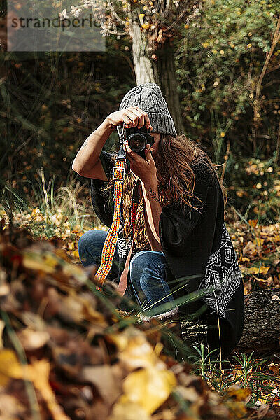 Mittlere erwachsene Frau beim Fotografieren mit Kamera im Wald im Herbst