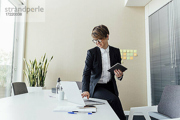 Geschäftsfrau  die einen Laptop benutzt und ein digitales Tablet am Schreibtisch im Büro hält