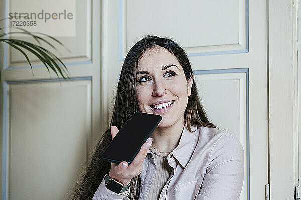 Lächelnde Frau  die ein Smartphone benutzt  um zu Hause Sprachnachrichten zu versenden