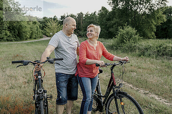 Lächelndes reifes Paar mit Fahrrad auf einem Feld