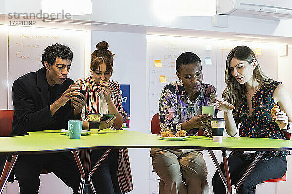 Geschäftsleute benutzen ihr Mobiltelefon beim Essen im Büro