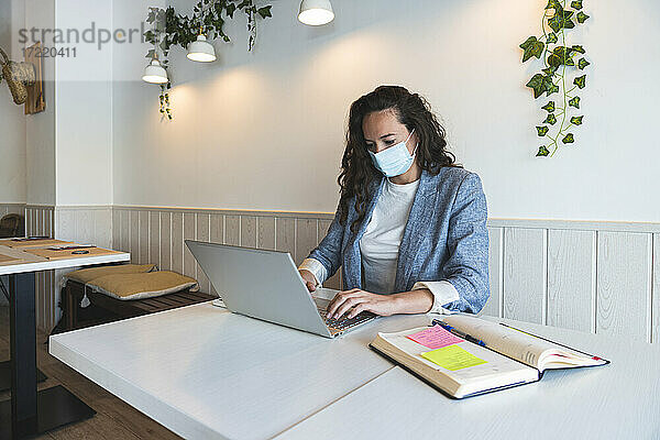 Freiberufliche Mitarbeiterin mit Laptop in einem Café während der COVID-19