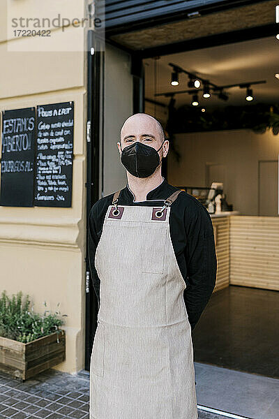 Männlicher Geschäftsinhaber mit Gesichtsschutzmaske vor einem Restaurant