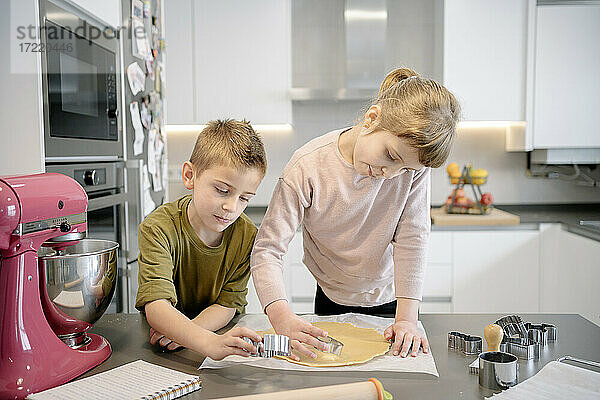 Mädchen und Junge verwenden Ausstechformen für Teig in der Küche