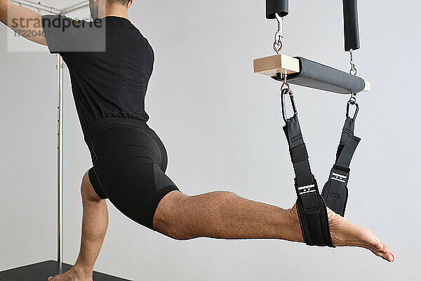 Mann streckt sein Bein beim Pilates auf dem Trapez im Übungsraum
