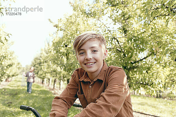 Blonder Junge lächelt  während er im Obstgarten sitzt