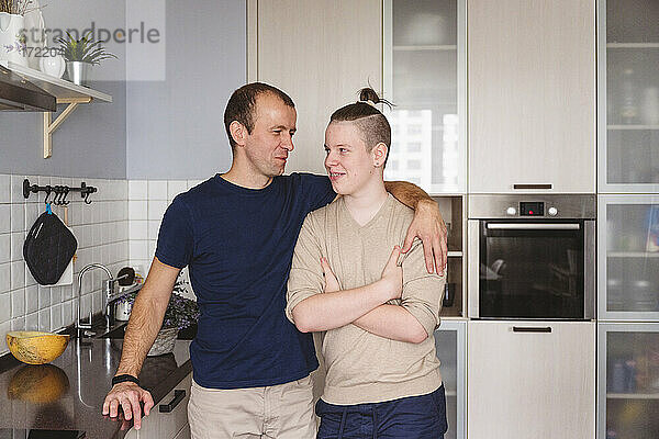 Vater umarmt Sohn im Teenageralter  während er zu Hause in der Küche steht