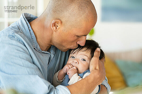 Mid erwachsenen Vater küsst sein Baby auf die Stirn im Wohnzimmer