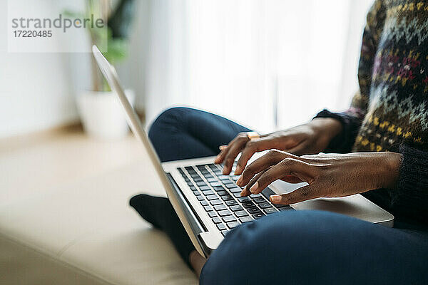Weibliche Fachkraft tippt auf einem Laptop  während sie im Wohnzimmer zu Hause arbeitet