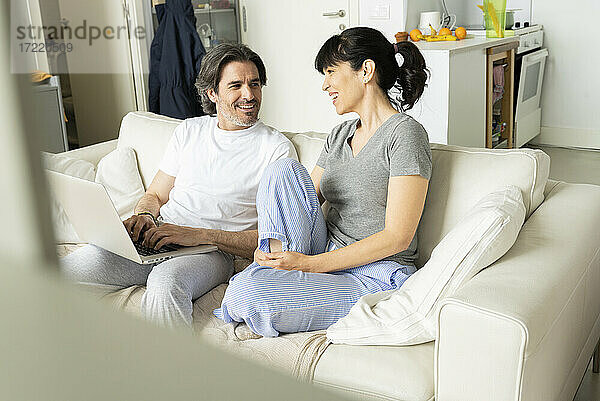 Mann mit Laptop im Gespräch mit Frau auf dem Sofa im Wohnzimmer zu Hause