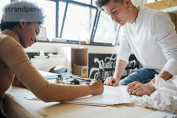 Junger Mann betrachtet eine Frau  die Kalligraphie übt  während er an einem Tisch im Atelier sitzt