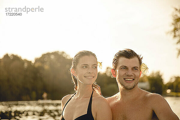Junges Paar mit Getränkeschirmen in den Haaren  die sich am See vergnügen