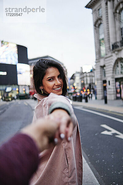 Glückliche Frau hält die Hand ihres Freundes auf der Straße in der Stadt