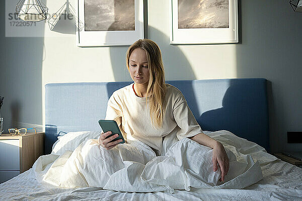 Frau benutzt Mobiltelefon  während sie zu Hause auf dem Bett sitzt