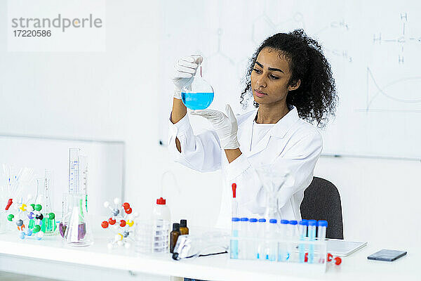 Junge Chemikerin  die eine Flüssigkeit in einem Kolben im Labor untersucht