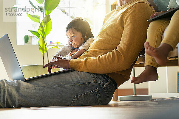 Vater arbeitet am Laptop  während er neben seinen Töchtern im Heimbüro sitzt