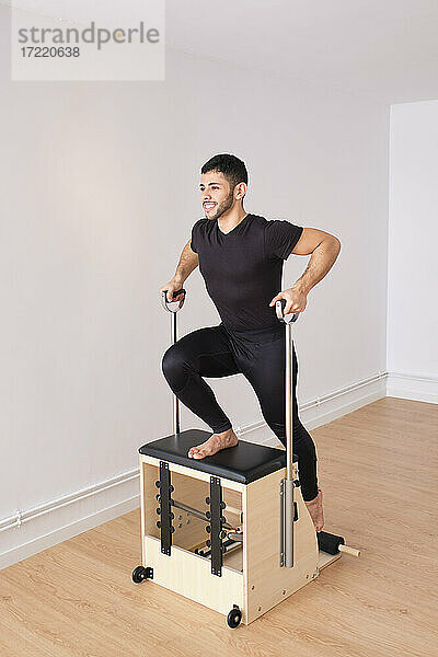 Mittlerer erwachsener Mann  der sich beim Pilates auf einem Stuhl im Übungsraum dehnt