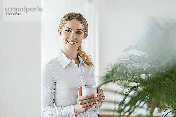 Lächelnd schöne weibliche professionelle hält Kaffeebecher im Büro
