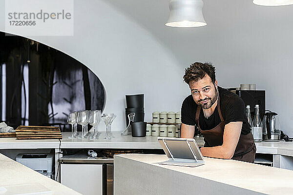 Selbstbewusster Chefkoch vor digitalem Tablet in der Restaurantküche