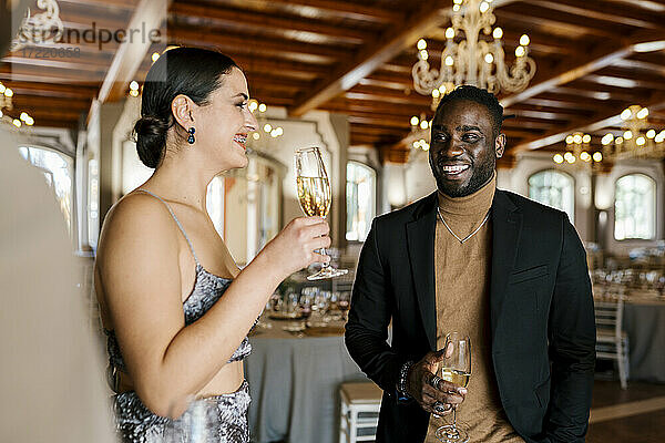 Schöne junge Frau im Gespräch mit männlichen Freunden beim Trinken von Champagner bei einem Bankett