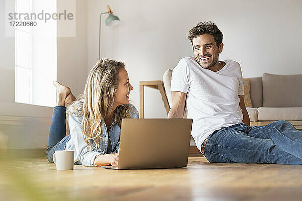 Entspannte Frau mit Laptop  die ihren lächelnden Freund zu Hause ansieht