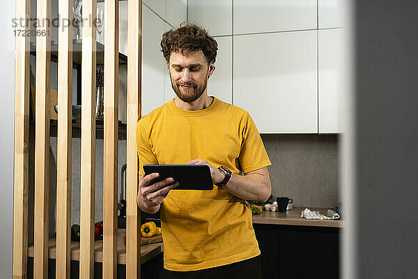 Gut aussehender Mann  der ein digitales Tablet benutzt  während er in der heimischen Küche steht