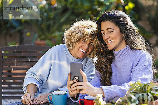 Lächelnde junge Frau nimmt Selfie mit reifen weiblichen durch Handy im Hinterhof