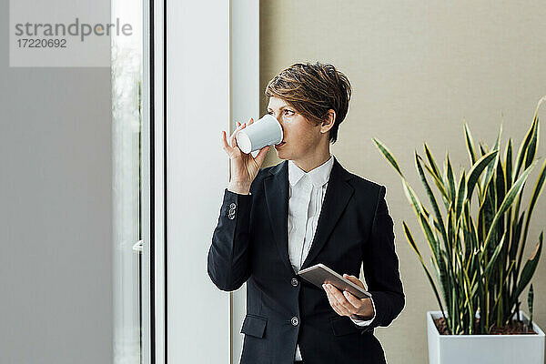 Nachdenkliche Unternehmerin mit digitalem Tablet bei einem Kaffee im Büro