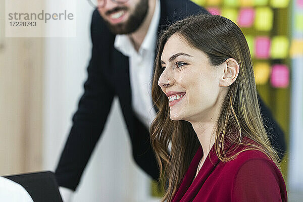 Geschäftsfrau lächelnd mit Kollege im Hintergrund im Büro