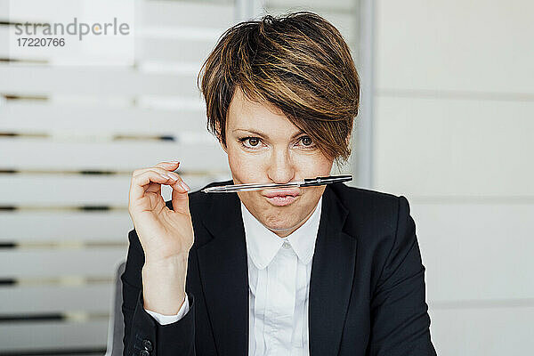 Verspielte Unternehmerin  die einen Stift auf den Lippen balanciert  während sie im Büro sitzt