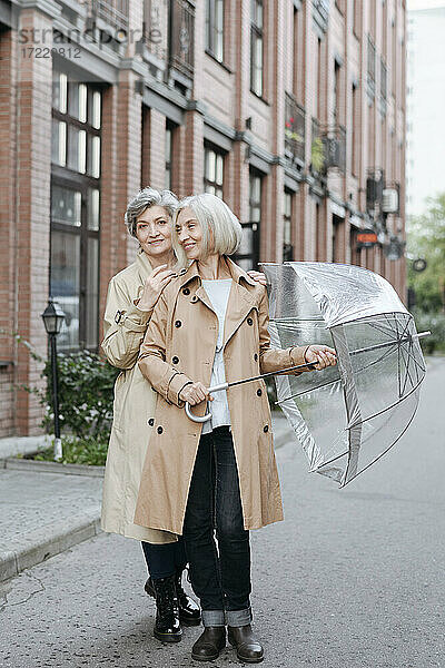 Lächelnde reife Freundinnen mit Regenschirm auf der Straße