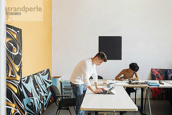 Hipster-Mann mit Laptop  während junge Frau am Tisch im Studio übt