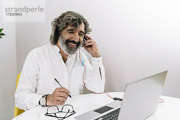 Mann hält Headset während eines Videogesprächs am Laptop im Büro
