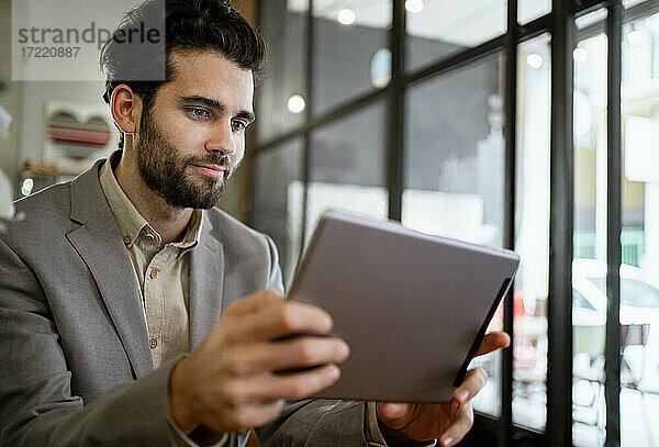 Mittlerer erwachsener Geschäftsmann  der in einem Café an einem digitalen Tablet arbeitet