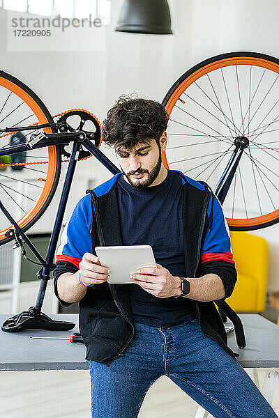 Mann  der ein digitales Tablet benutzt  während er sich zu Hause auf einen Tisch mit einem umgestürzten Fahrrad stützt