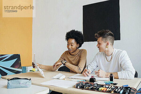 Junges multiethnisches Paar  das im Atelier sitzend über Kalligrafie-Schrift diskutiert