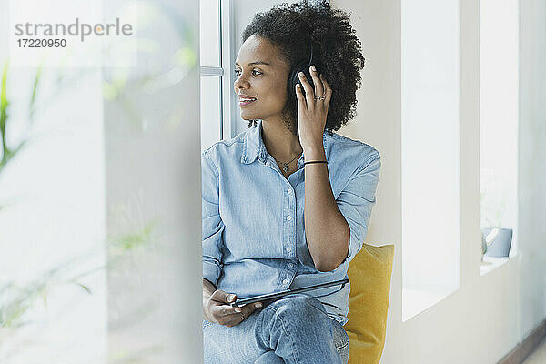 Frau stellt Kopfhörer ein  während sie zu Hause mit einem digitalen Tablet sitzt