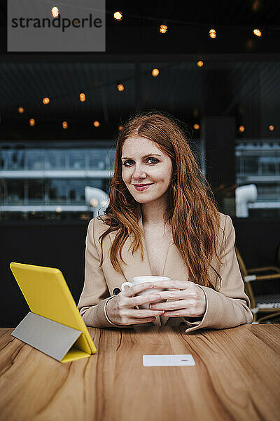 Lächelnde schöne Frau mit roten Haaren sitzt am Tisch in einem Cafe