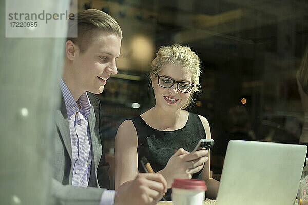 Lächelnde Unternehmerin  die mit ihrem Mobiltelefon SMS schreibt  während sie neben einem Geschäftsmann sitzt