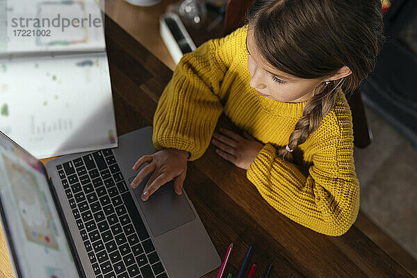 Mädchen im gelben Pullover e-learning über Laptop zu Hause