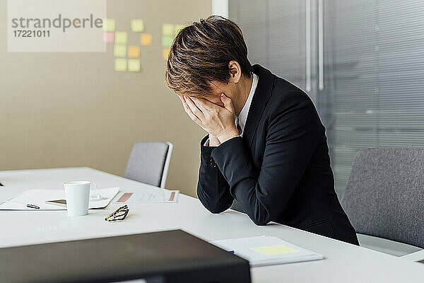 Überarbeitete Geschäftsfrau mit dem Kopf in den Händen sitzt am Schreibtisch im Büro
