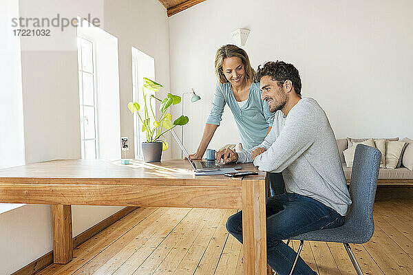 Schöne Frau  die einen Mann ansieht  der an einem Laptop arbeitet  während er auf einem Schreibtisch im Büro zu Hause sitzt