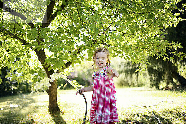 Glückliches Mädchen gestikuliert  während sie ein Bewässerungsrohr im Garten hält