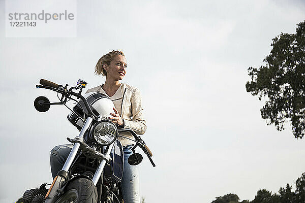 Schöne Bikerin mit Helm auf dem Motorrad  die vor dem Himmel wegschaut