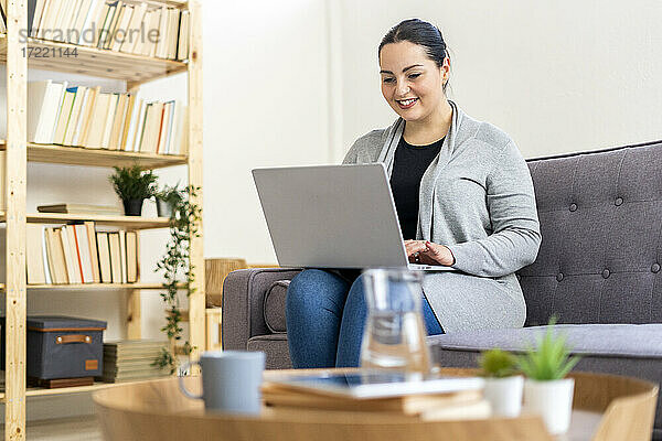 Lächelnde Frau mit Laptop im Wohnzimmer zu Hause