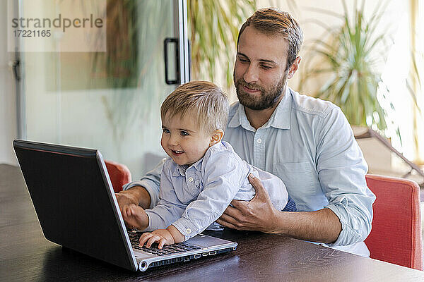 Lächelnder süßer Junge  der einen Laptop vor seinem Vater am Tisch benutzt