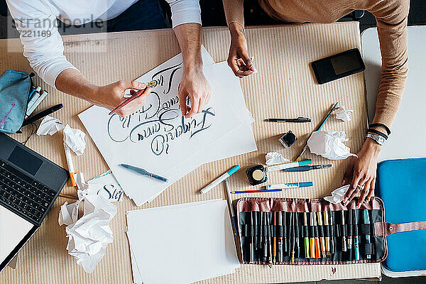 Junges multiethnisches Paar  das in einem Atelier gemeinsam an einer kalligrafischen Schrift arbeitet