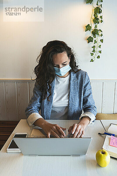 Geschäftsfrau arbeitet in einem Café während einer Pandemie an einem Laptop