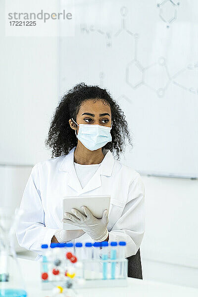 Eine Forscherin schaut weg  während sie ein digitales Tablet im Labor während COVID-19 hält