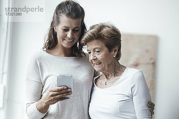 Lächelnde Frau  die das Smartphone ihrer Großmutter zu Hause benutzt